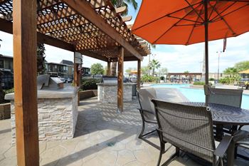 A patio with a table and chairs under an orange umbrella at Willow Creek Apartments, Houston